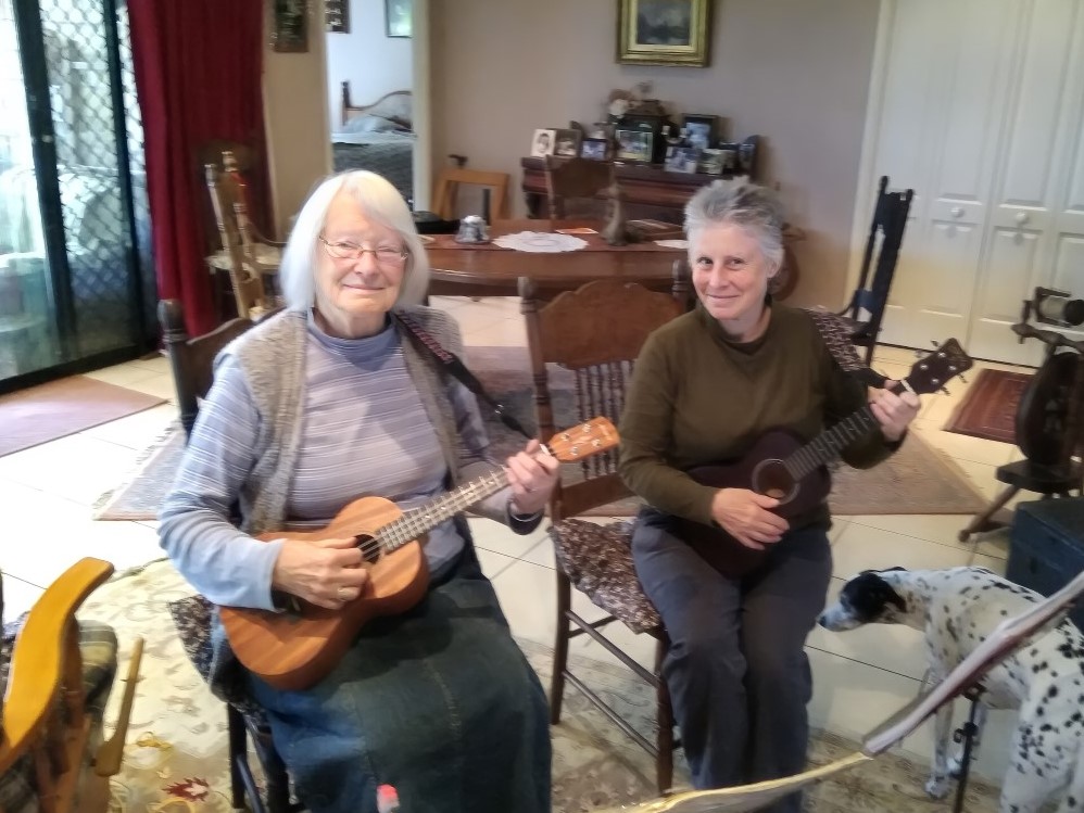Two senior ladies sitting in a living room and playing ukuleles