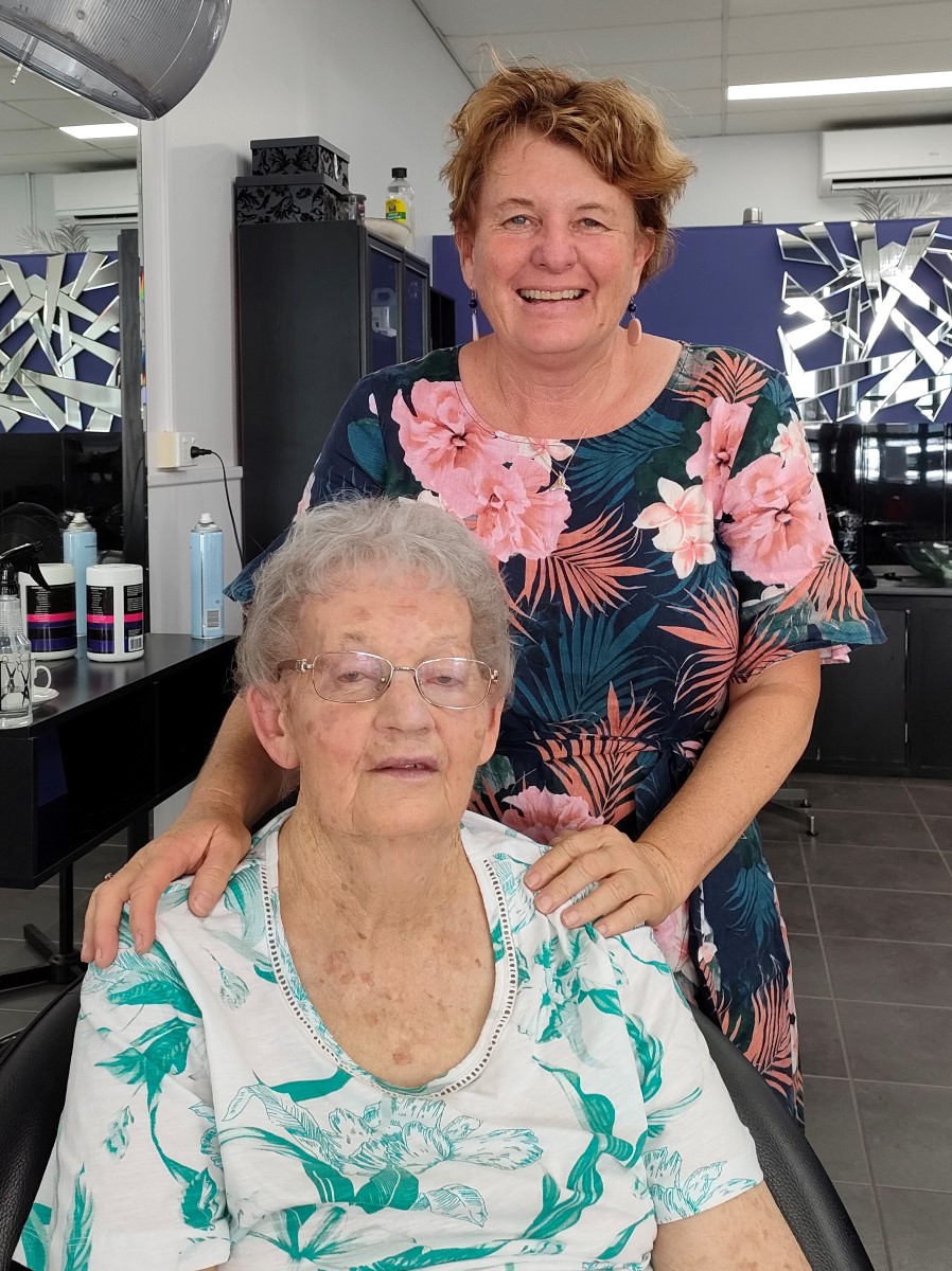Middle aged woman standing behind seated senior lady with her hands on her shoulder at a hairdresser's