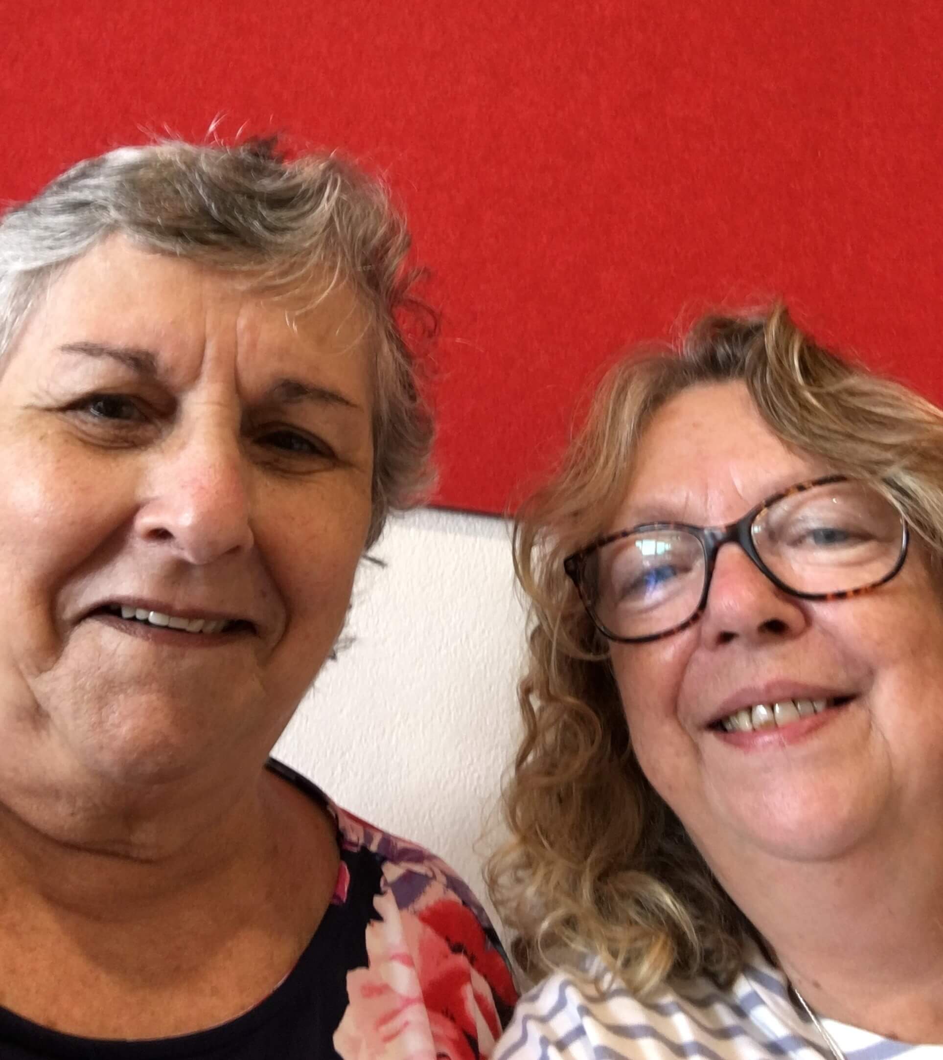 Selfie of two older ladies in front of a red wall