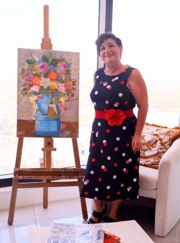 older woman in spotty dress with a painting of flowers.